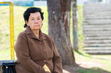 Hispanic grandmother sitting by bench wearing brown jacket