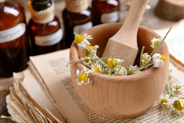 Old book with dry flowers in mortar and bottles on table close up