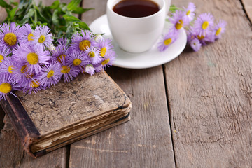 Old book with beautiful flowers and cup of tea on wooden table close up