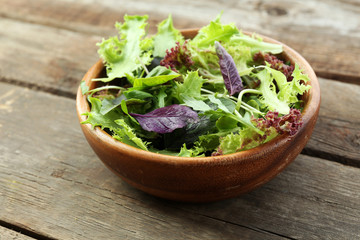 Fresh mixed green salad in bowl on wooden table close up