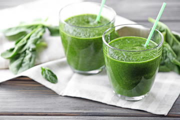 Glasses of spinach juice with napkin on wooden table, closeup