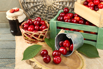 Sweet cherries with green leaves in bucket and wooden boxes, on wooden background