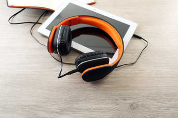 Headphones with tablet on wooden table close up