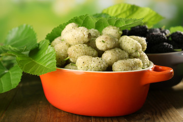 Ripe mulberries in bowls with green leaves on table close up