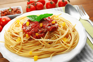 Spaghetti with tomato sauce, paprika and cheese on white plate, on color wooden background