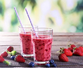 Glasses of berry smoothie on wooden table on blurred background