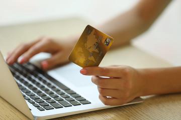 Female hands holding credit card with laptop on table close up