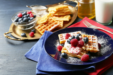 Sweet homemade waffles with forest berries and cream on plate, on dark wooden background