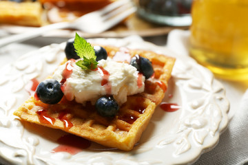 Sweet homemade waffles on plate, on color wooden background
