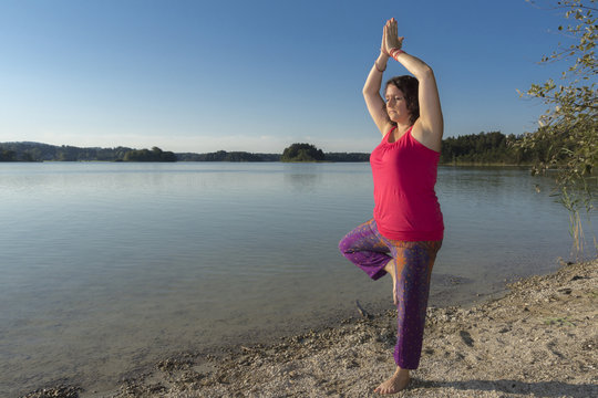 Junge Yogine am See übt Baumfigur bei Yoga