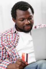 African American man with laptop and credit card in room