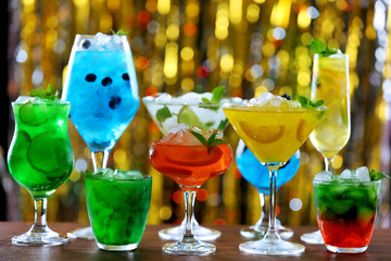Glasses of cocktails with ice on blurred lights background
