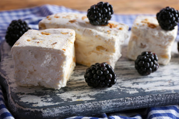 Sweet nougat with nuts and blackberries on cutting board close up