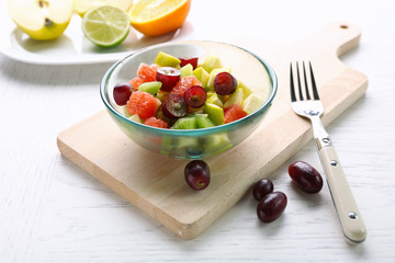 Fruit salad in glass bowl, on light wooden background