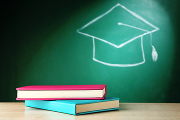 Stack of books and bachelor hat drawing on blackboard background