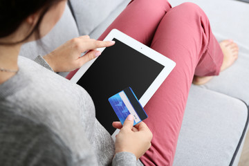 Concept for Internet shopping: woman with digital tablet and credit card sitting on sofa, at home