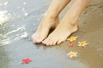 Female legs with sea stars on sand beach