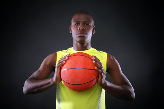 African American basketball player holding ball on dark background