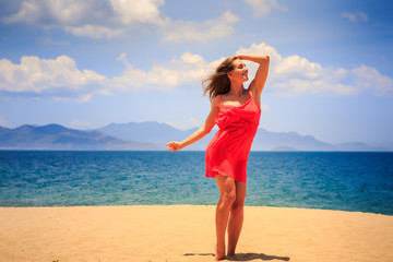 blond girl in red stands on sand touches head and looks upwards