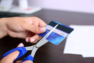 Woman's hands cutting bank card with scissors on wooden table background
