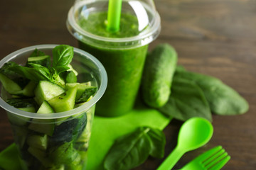Green vegetable and fruit salad and healthy fresh drink in plastic cups on wooden background. Colorful diet concept