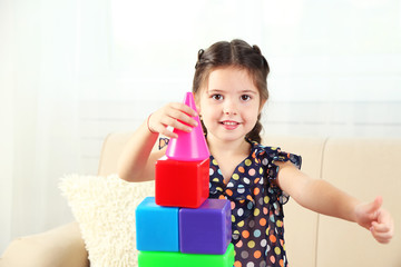 Little girl playing with cubes on home interior background