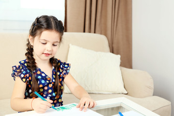 Cute little girl drawing picture on home interior background