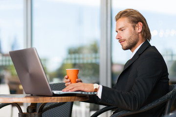     Handsome businessman enjoying a cup of coffee and using his laptop