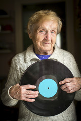 Elderly lady is holding a vinyl record. With place for your text on disk.
