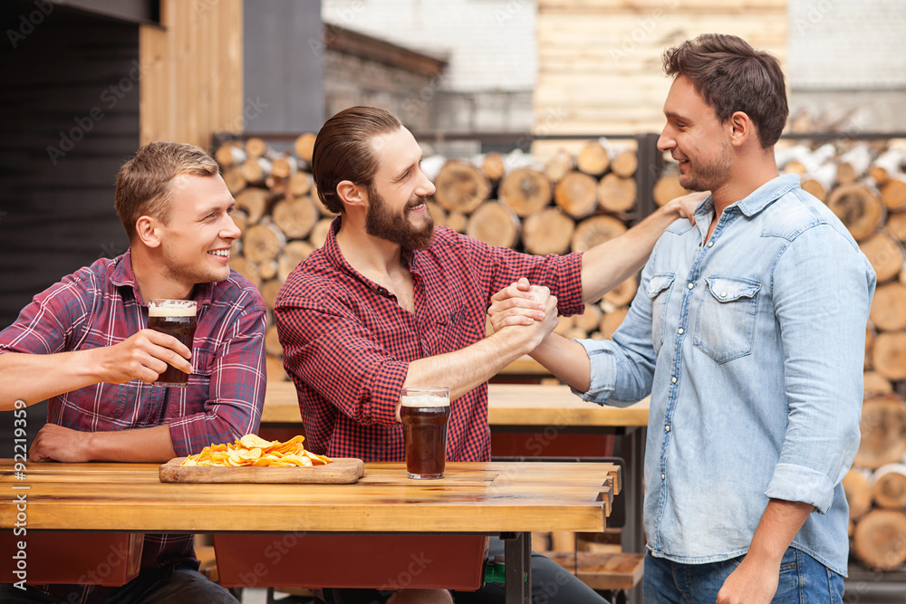 Wall mural Attractive young guys are greeting in beerhouse