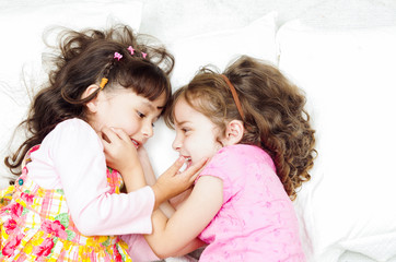 Young adorable hispanic sisters lying down playing and embracing