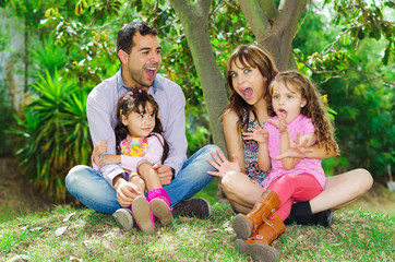 Fototapeta premium Beautiful hispanic family of four sitting outside on grass
