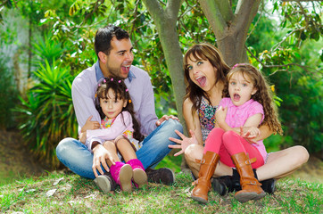 Beautiful hispanic family of four sitting outside on grass