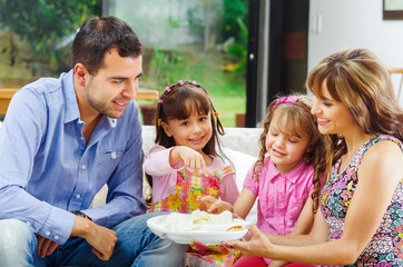 Hispanic parents with two daughters eating from a tray of potato