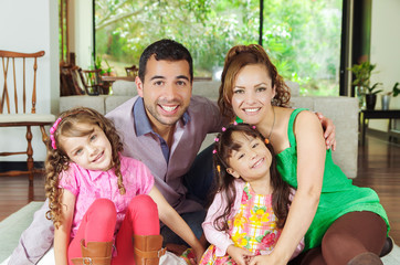 Beautiful hispanic family of four sitting on floor in livingroom
