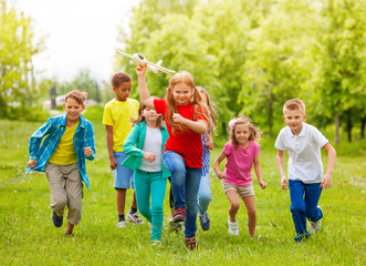 Obraz premium Moving girl holds airplane toy and kids behind