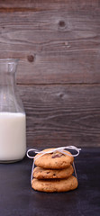 Stack of Chocolate chip cookie and bottle of milk on black backg