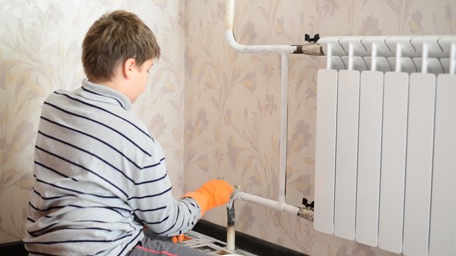 Boy paints a heating radiator in  apartment