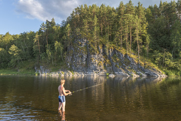 Fototapeta na wymiar Рыбак ловит рыбу в реке удочкой.