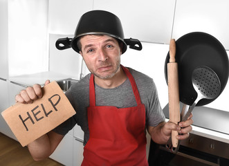 funny man holding pan with pot on head in apron at kitchen asking for help