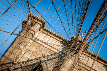Naklejka premium Closeup of the Brooklyn Bridge in New York City, USA. The American flag is flying over the cloudless blue sky