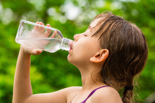 Child drinking clean tap water from transparent plastic bottle