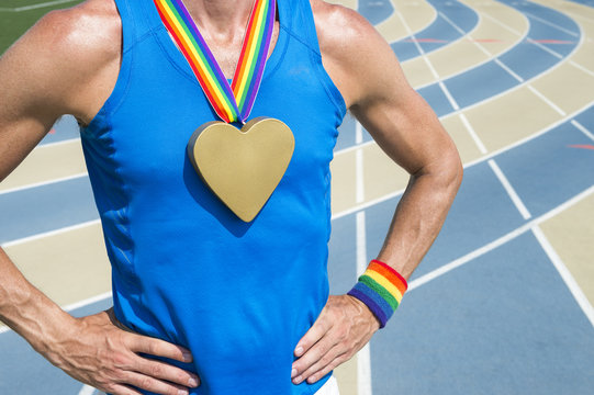 Gay athlete standing with heart gold medal and rainbow ribbons at a running track