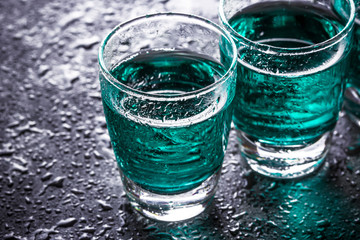 Colorful vodka shots on wet black surface.