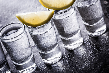 Vodka shot glass on black wet surface.