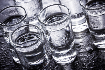 Vodka shot glass on wet black surface.