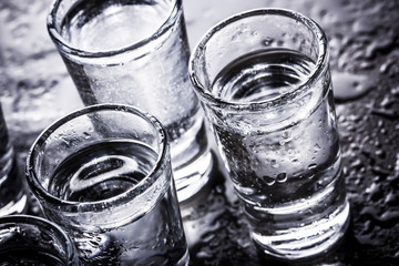 Vodka shot glass on wet black surface.