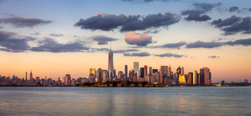 Lower Manhattan skyscrapers before sunset with One World Trade Center. Ellis Island appears in front of New York City’s Financial District.