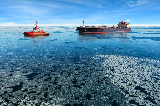 Red tugboat towing a tanker ship at winter.