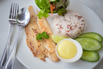 brow rice grilled fish and salad in white dish